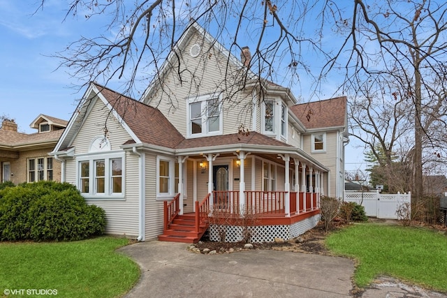 victorian home featuring fence, covered porch, and a front lawn