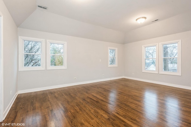empty room featuring dark wood-type flooring, visible vents, vaulted ceiling, and baseboards
