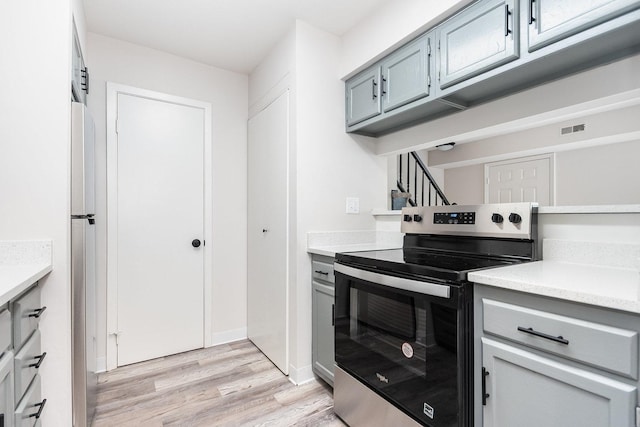 kitchen featuring stainless steel electric range oven, gray cabinetry, light countertops, and light wood-style flooring
