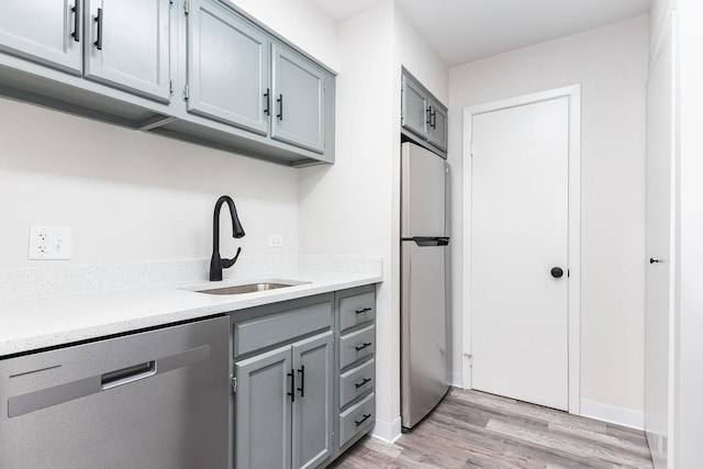 kitchen featuring a sink, appliances with stainless steel finishes, light countertops, light wood-type flooring, and gray cabinets