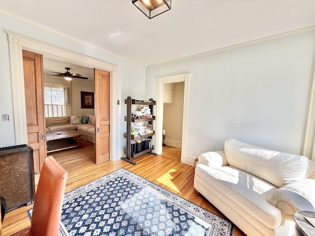 living room with ornamental molding, ceiling fan, light wood-style flooring, and baseboards