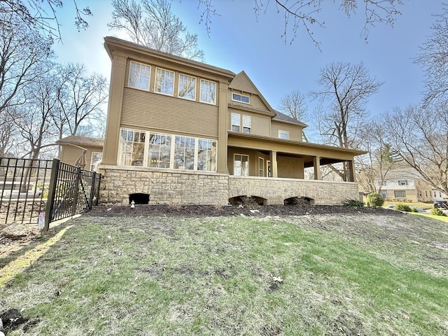 back of house with a gate, fence, a yard, and stone siding