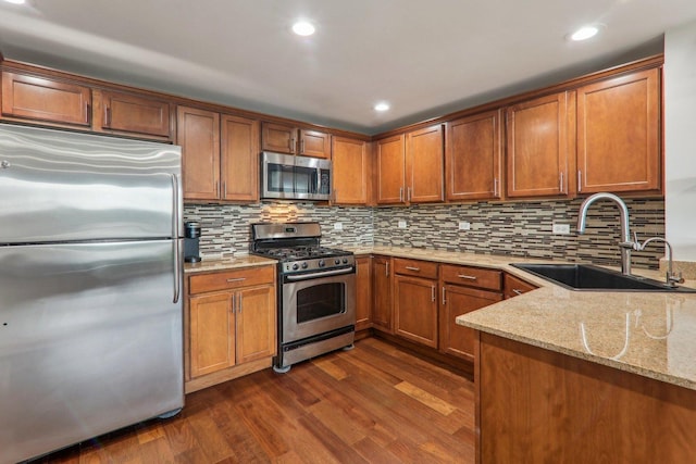 kitchen featuring light stone counters, decorative backsplash, a sink, stainless steel appliances, and dark wood finished floors