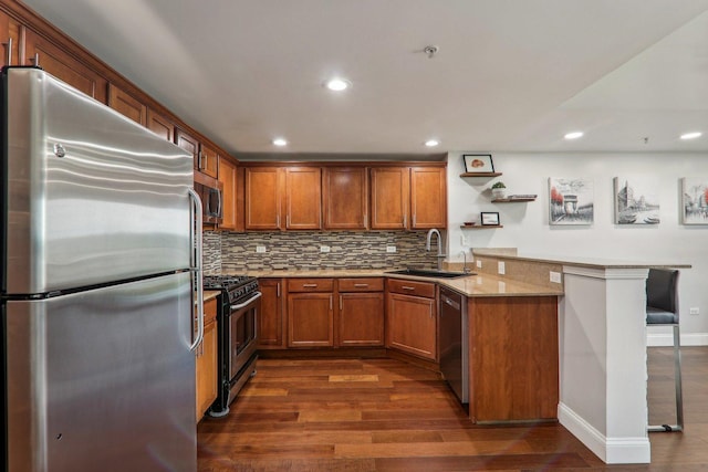 kitchen featuring recessed lighting, brown cabinets, a sink, a peninsula, and appliances with stainless steel finishes