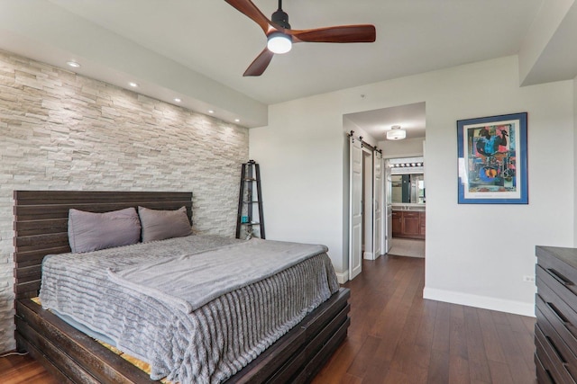 bedroom featuring connected bathroom, hardwood / wood-style flooring, ceiling fan, a barn door, and baseboards