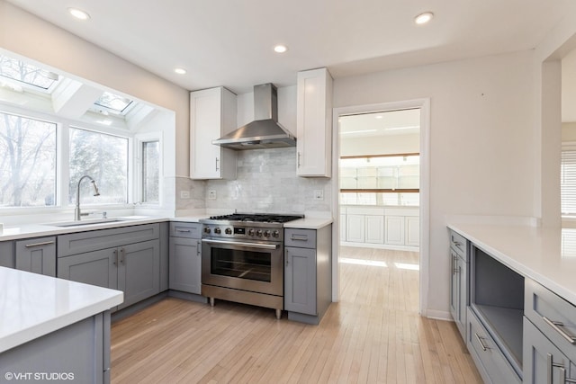 127 Riverside Dr, Northfield, IL 60093 - kitchen featuring a sink, gray cabinets, wall chimney range hood, stainless steel stove, and a skylight