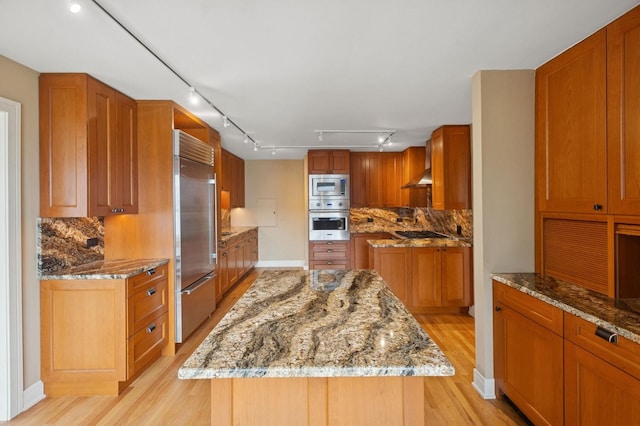 247 E Chestnut St Unit 2303, Chicago, IL 60611 - kitchen featuring built in appliances, backsplash, light wood-style floors, brown cabinetry, and rail lighting