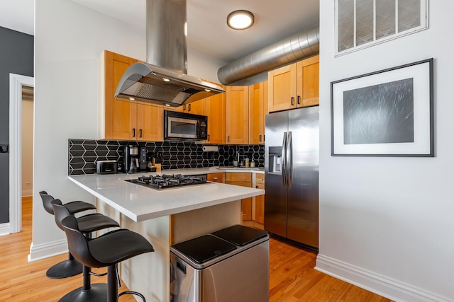 kitchen featuring a kitchen breakfast bar, stainless steel appliances, island range hood, backsplash, and visible vents