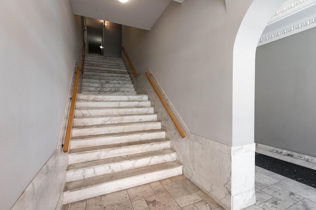 stairs with arched walkways and a wainscoted wall