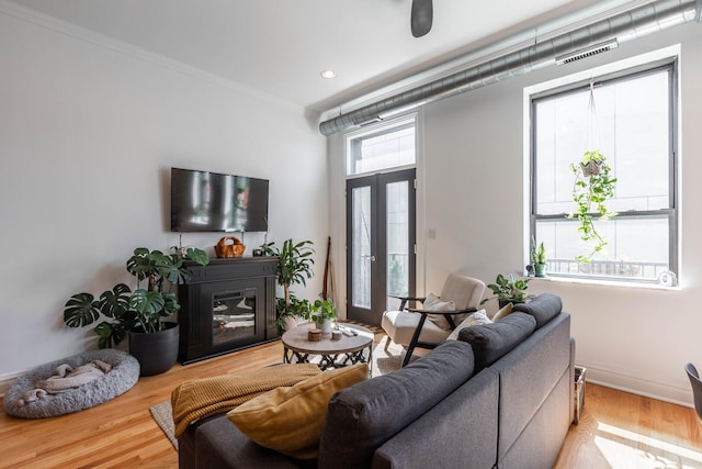 living room featuring crown molding, a glass covered fireplace, baseboards, wood finished floors, and visible vents