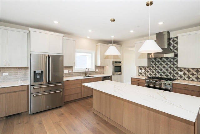 kitchen with a sink, decorative backsplash, wall chimney exhaust hood, appliances with stainless steel finishes, and hardwood / wood-style flooring
