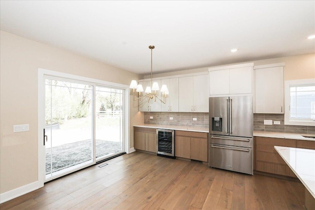 kitchen featuring light countertops, high end fridge, wood-type flooring, an inviting chandelier, and wine cooler