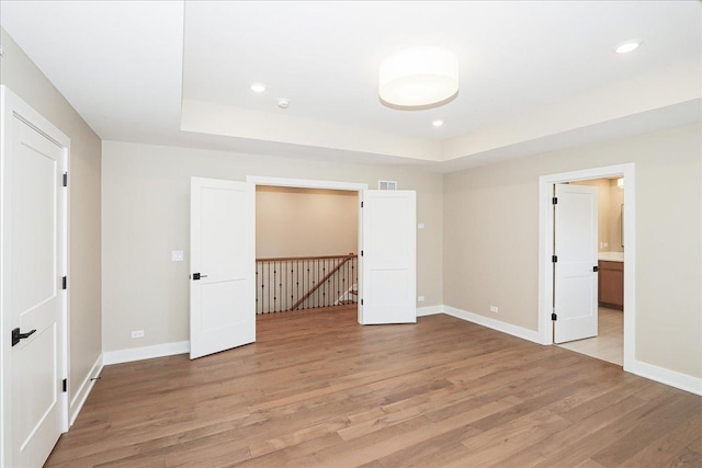 empty room with a tray ceiling, light wood-style flooring, recessed lighting, and baseboards