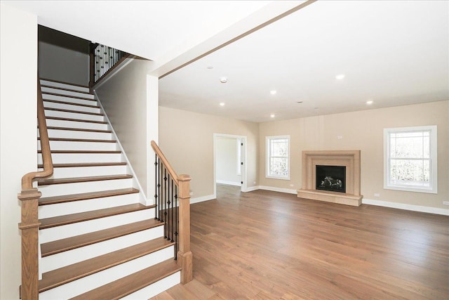unfurnished living room with stairway, baseboards, recessed lighting, a fireplace, and wood finished floors