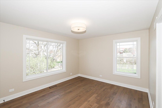 unfurnished room featuring a wealth of natural light, visible vents, dark wood-style floors, and baseboards