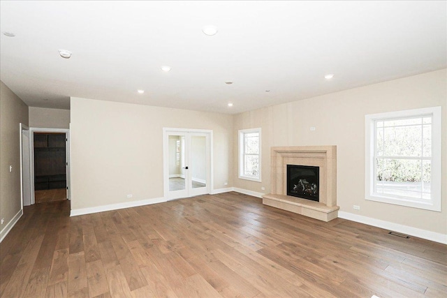 unfurnished living room featuring wood finished floors, a high end fireplace, baseboards, visible vents, and french doors