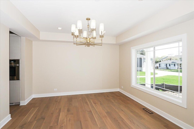 unfurnished dining area featuring an inviting chandelier, wood finished floors, visible vents, and baseboards