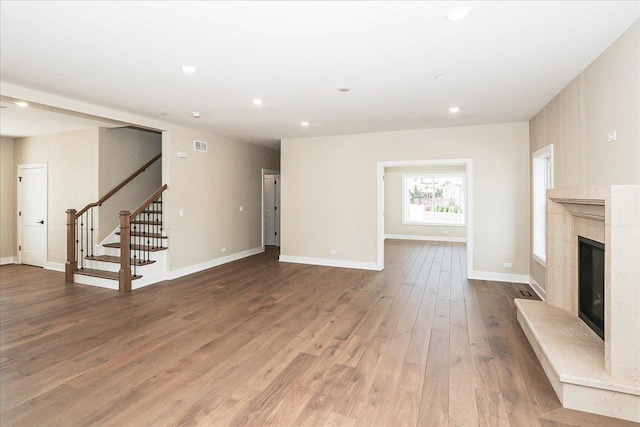 unfurnished living room featuring a high end fireplace, stairway, wood finished floors, and baseboards