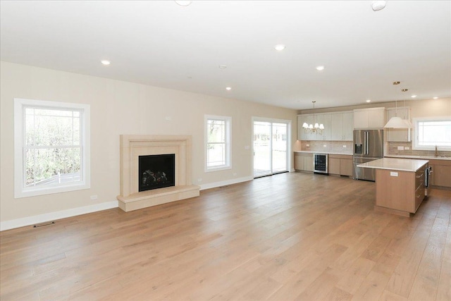 unfurnished living room with light wood-style flooring, beverage cooler, visible vents, baseboards, and a fireplace