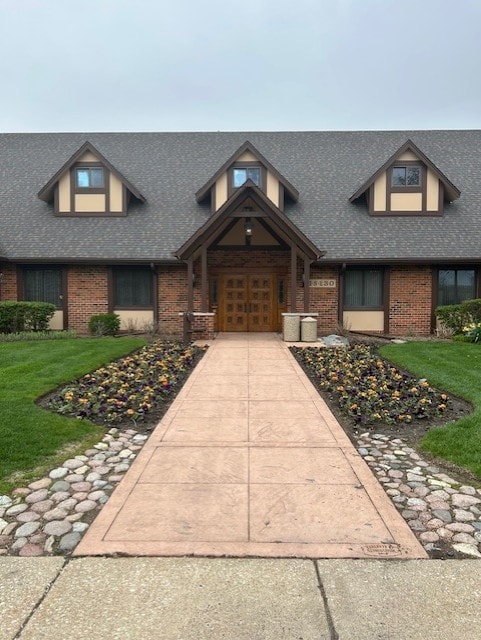 view of front of property featuring brick siding, a shingled roof, and a front yard