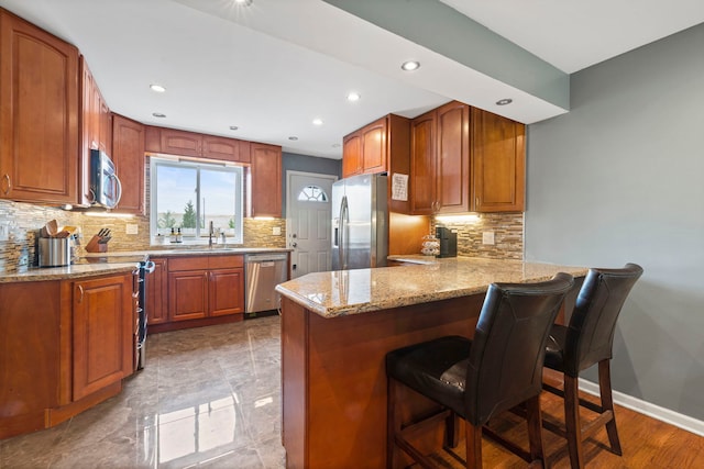 kitchen with light stone countertops, a peninsula, stainless steel appliances, and decorative backsplash