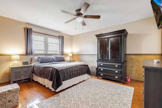 bedroom featuring ceiling fan, a wainscoted wall, and hardwood / wood-style floors
