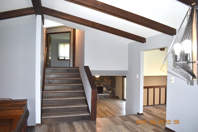 stairway with vaulted ceiling with beams, a stone fireplace, and wood finished floors