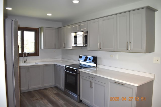 kitchen featuring gray cabinetry, appliances with stainless steel finishes, a sink, and dark wood-type flooring