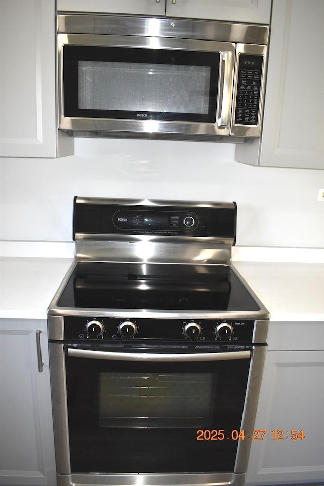 kitchen with light countertops, electric range oven, stainless steel microwave, and white cabinetry