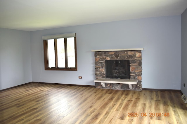 unfurnished living room with baseboards, a stone fireplace, and wood finished floors
