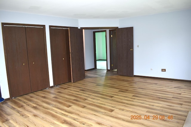 unfurnished bedroom with light wood-type flooring, multiple closets, and baseboards