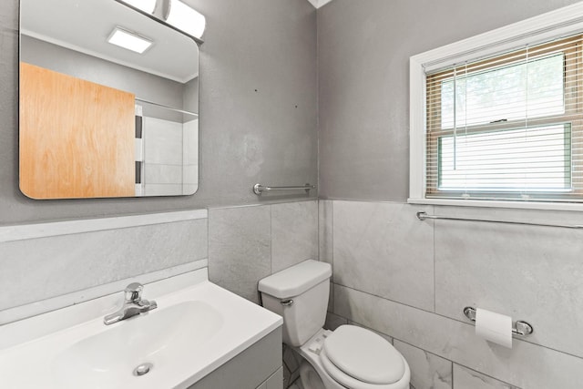 bathroom with tile walls, toilet, vanity, and wainscoting