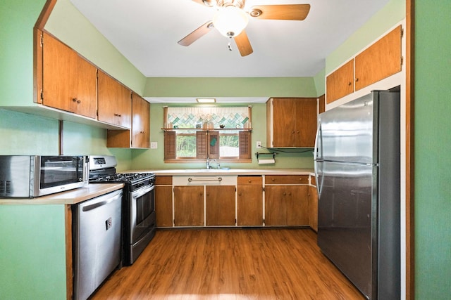 kitchen with appliances with stainless steel finishes, a sink, wood finished floors, brown cabinetry, and light countertops