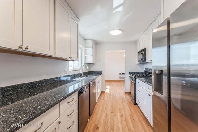 kitchen with light wood finished floors, a sink, stainless steel appliances, dark stone countertops, and white cabinetry