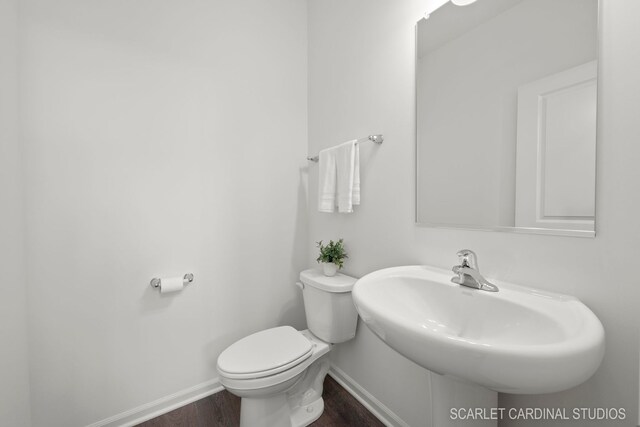 bathroom featuring toilet, a sink, wood finished floors, and baseboards