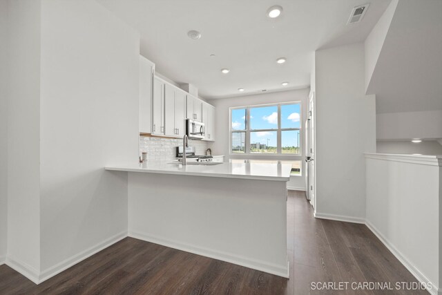 kitchen with white cabinetry, stainless steel appliances, light countertops, dark wood finished floors, and a peninsula