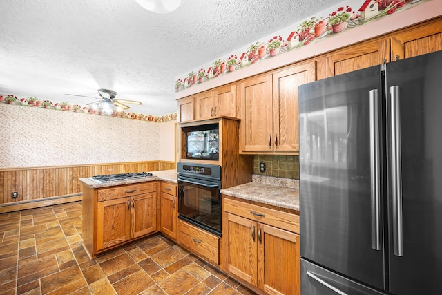 kitchen with a textured ceiling, light countertops, a wainscoted wall, black appliances, and a peninsula