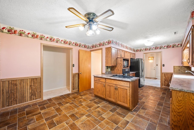 kitchen featuring wainscoting, ceiling fan, a textured ceiling, a sink, and appliances with stainless steel finishes