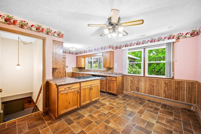 kitchen featuring ceiling fan, wainscoting, a textured ceiling, wood walls, and brown cabinetry