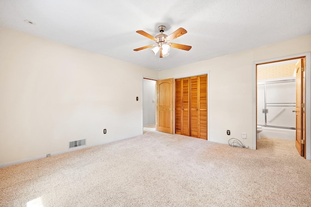 unfurnished bedroom featuring visible vents, carpet floors, a closet, connected bathroom, and a ceiling fan