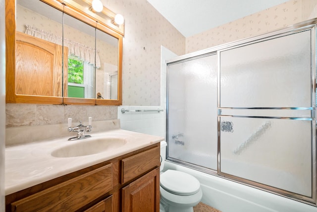 bathroom featuring vanity, bath / shower combo with glass door, a wainscoted wall, toilet, and wallpapered walls