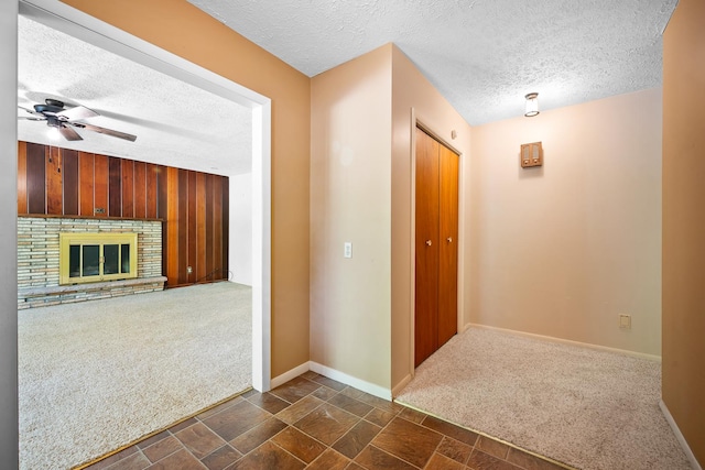 hall with stone finish floor, a textured ceiling, baseboards, dark colored carpet, and wooden walls