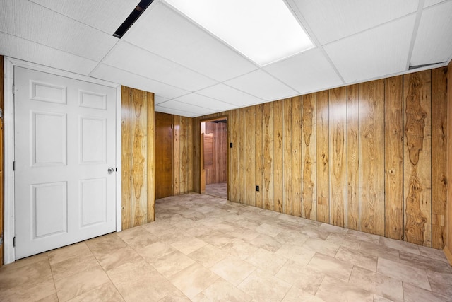 unfurnished room with wood walls and a drop ceiling