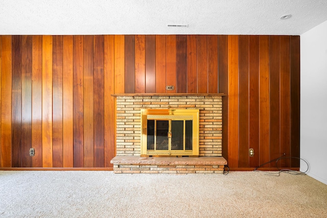 unfurnished living room featuring wooden walls, carpet floors, a brick fireplace, and a textured ceiling