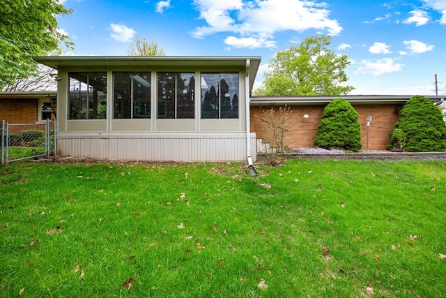 rear view of property featuring fence, a yard, a sunroom, and brick siding