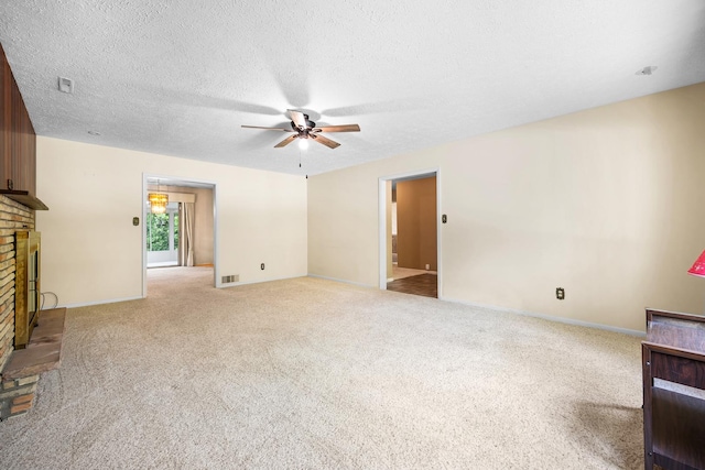 unfurnished living room featuring a brick fireplace, carpet floors, a textured ceiling, a ceiling fan, and visible vents