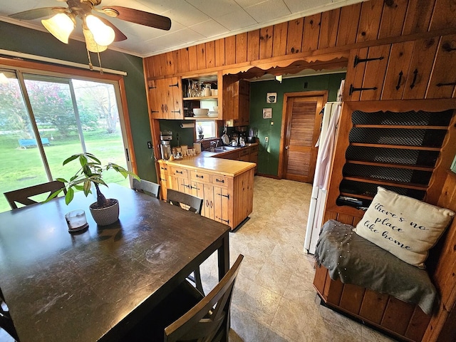 dining area featuring a ceiling fan, wooden walls, and crown molding