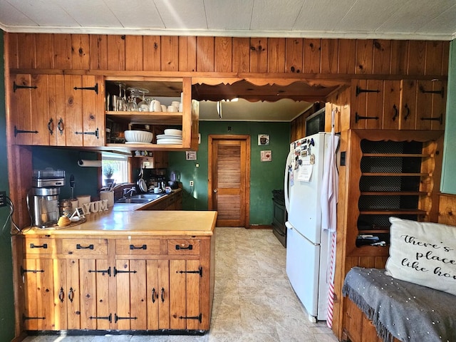 kitchen with wood walls, light countertops, freestanding refrigerator, and a sink
