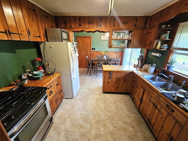 kitchen with a sink, a peninsula, appliances with stainless steel finishes, and brown cabinets