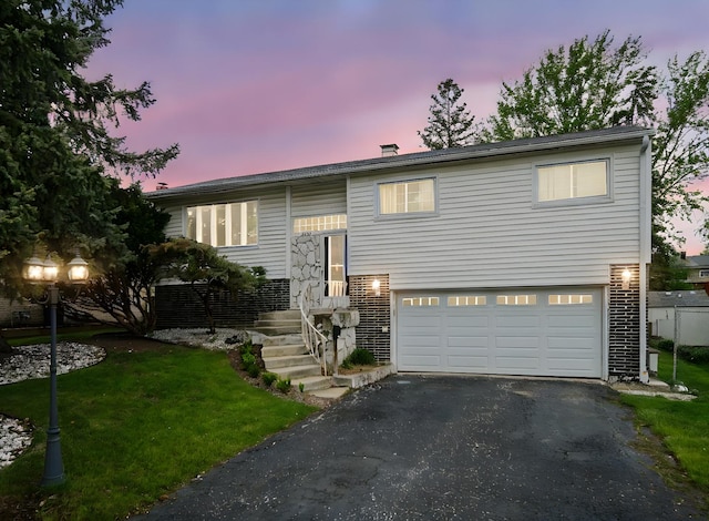 split foyer home with brick siding, a garage, aphalt driveway, and a front yard
